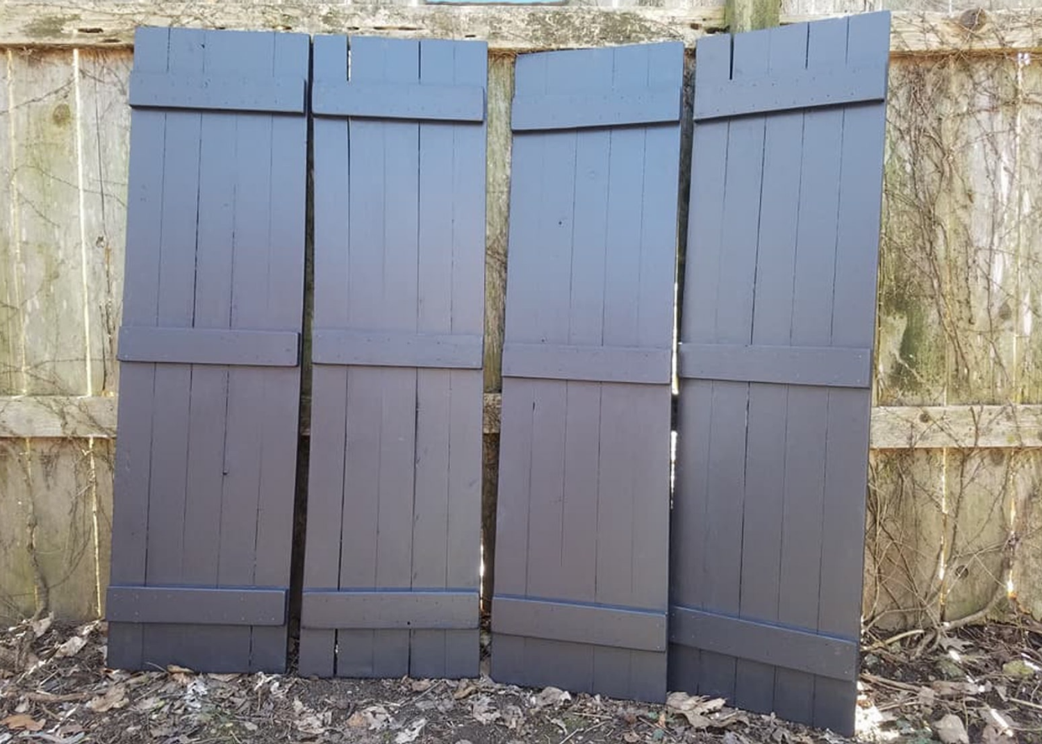 Four dark wooden boards leaned against a weathered fence, showcasing a rustic design with horizontal cross braces.