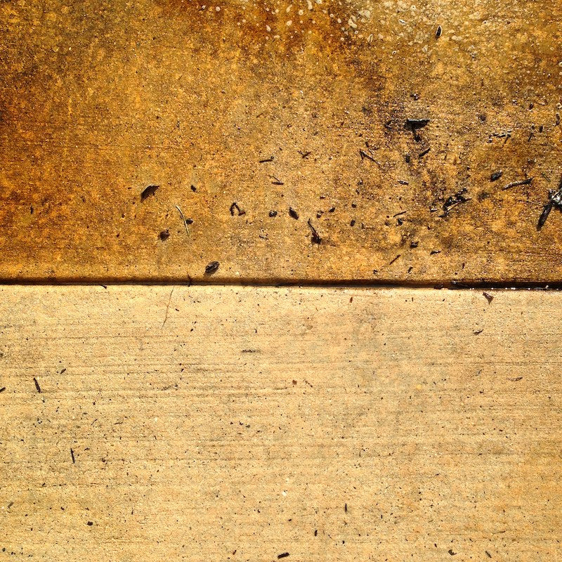 Close-up of a textured surface with rusted metal above and a concrete base below, scattered with small debris and dirt.