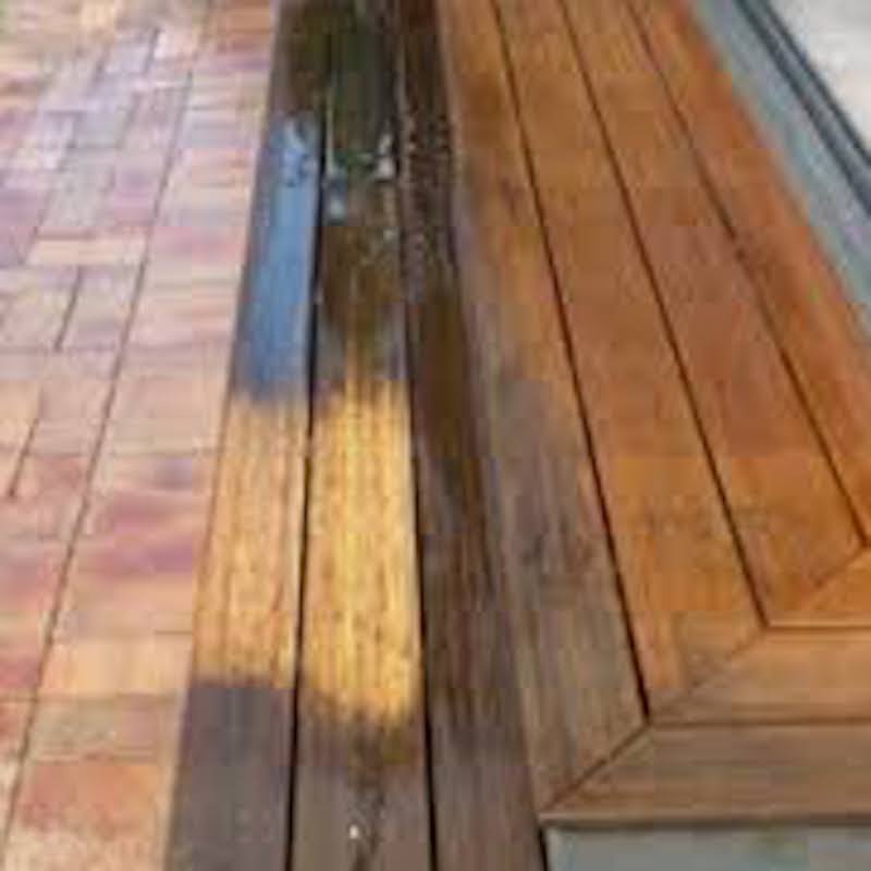 Close-up of wet wooden planks contrasting with dry, polished wood, showcasing rich colors and textures on a patio surface.