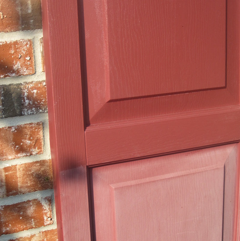 Close-up of a textured red wooden door adjacent to a rustic brick wall, showcasing the door's paneled design and warm hues.