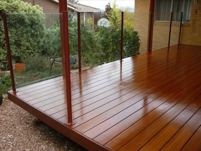 A polished wooden deck with glass balustrades, surrounded by greenery, showcasing a modern outdoor living space.