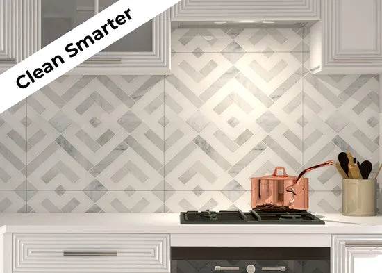 A modern kitchen scene featuring a white cabinet, decorative marble backsplash, and a shiny copper pot on the stove with wooden utensils nearby.