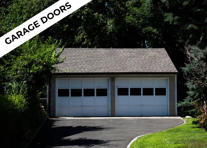 A white two-car garage with large windows, surrounded by lush greenery and a curved driveway on a sunny day. Text reads "Garage Doors".